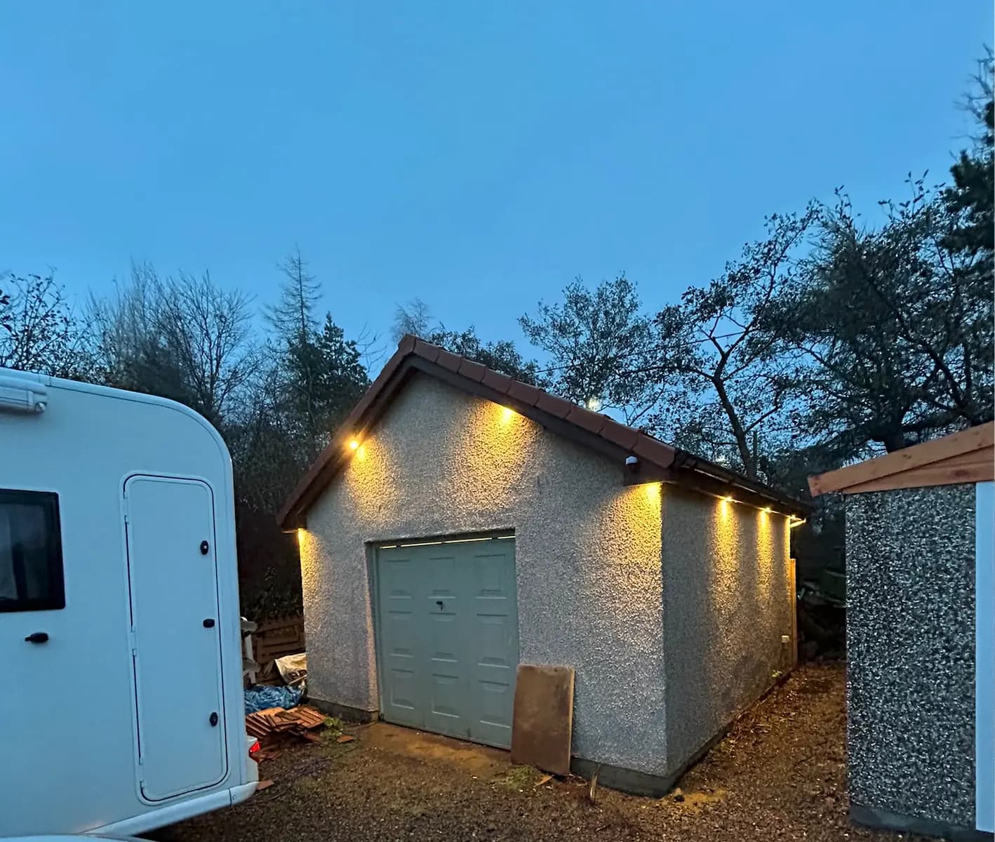 Detached garage illuminated by exterior downlights at dusk