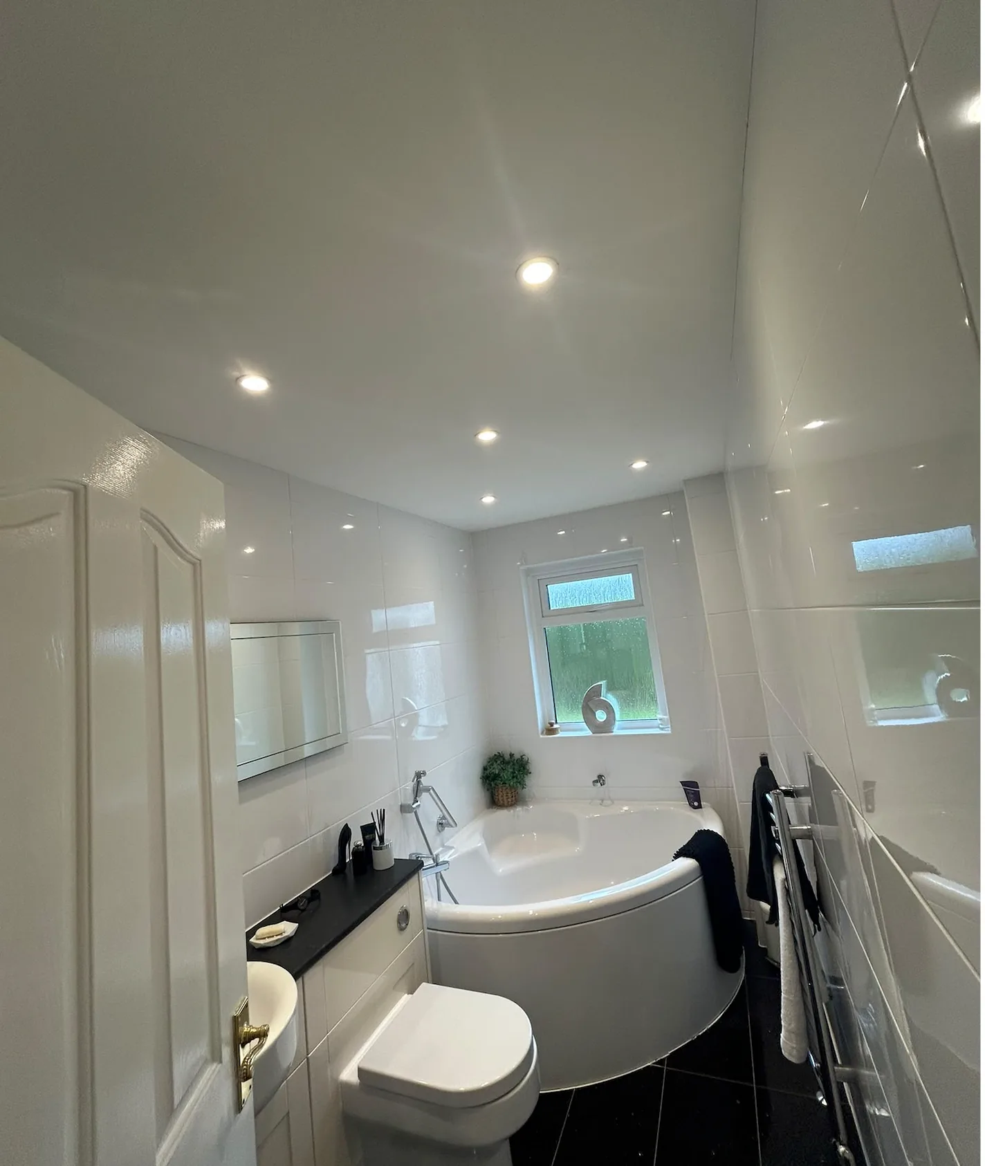 White tiled bathroom with recessed ceiling lights and a corner bath